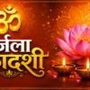 Nirjala Ekadashi devotional banner featuring a glowing golden Om symbol, elegant Hindi text, a pink lotus flower, three illuminated diya lamps, intricate golden mandala patterns, and an ornate decorative border on a saffron-orange background.